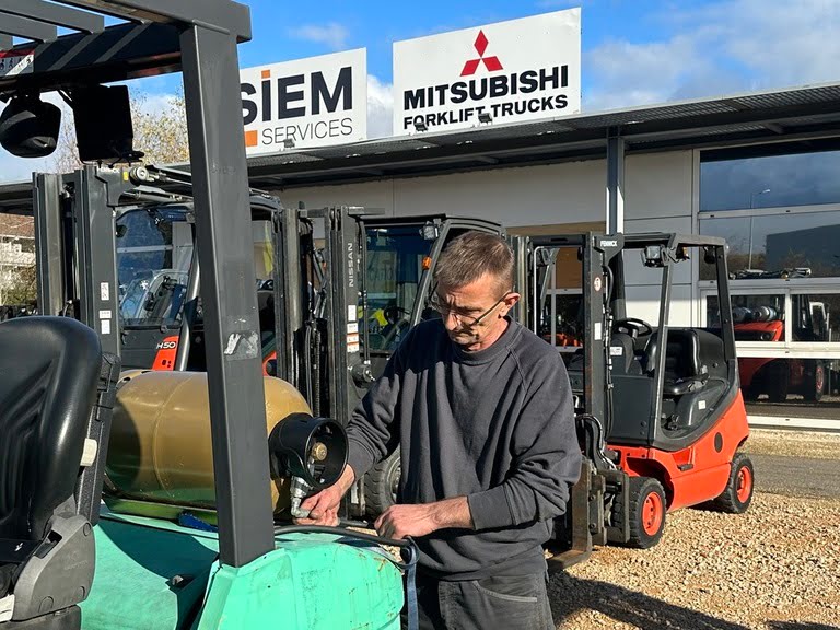 Photo d'un technicien effectuant le remplacement d'un flexible hydraulique sur une bouteille de gaz placée à l'arrière d'un chariot élévateur