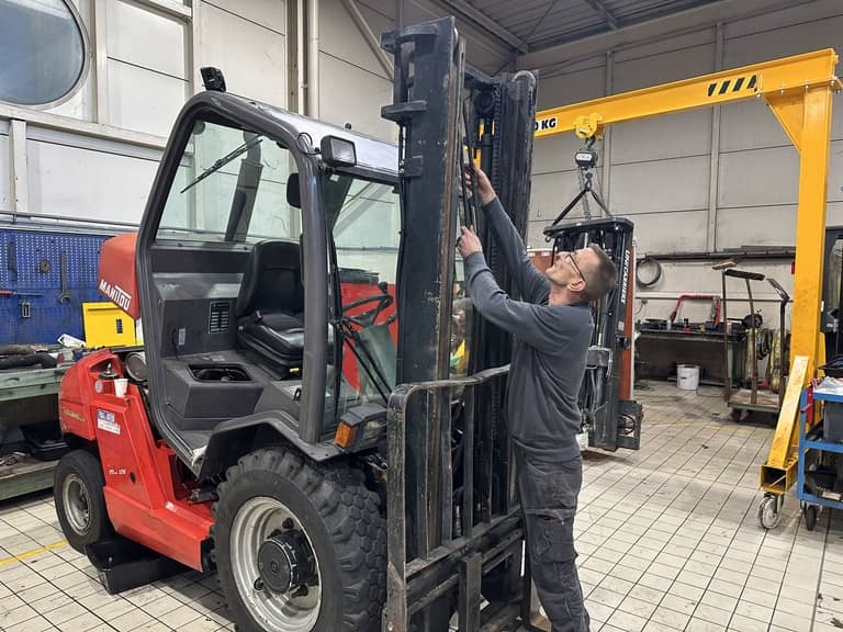 Photo d'un technicien de manutention en cours de remplacement d'un flexible hydraulique sur le mât d'un chariot élévateur