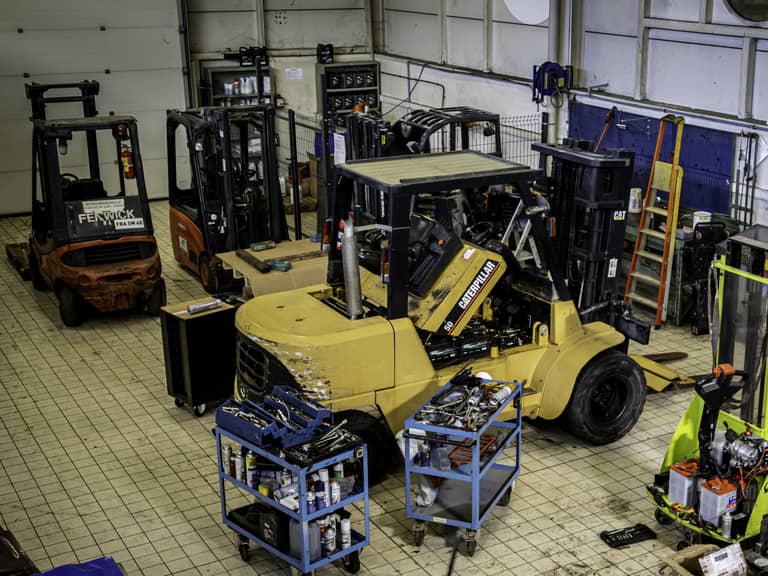 Photographie d'un atelier où un chariot élévateur gros tonnage Caterpillar est en cours de réparation, entouré de chariots élévateurs Hangcha et Fenwick