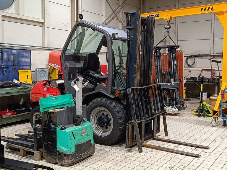 Un chariot élévateur frontal Manitou et un transpalette électrique Mitsubishi Forklift en réparation dans un atelier